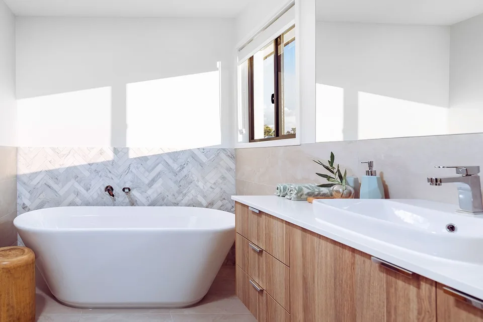 Modern bathroom featuring a freestanding bath, chevron tiled feature wall, and warm timber accents.
